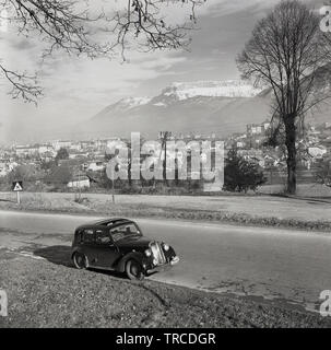 1950, historische, ein Auto der Ära auf einer Straße außerhalb der französischen Stadt Sisteron mit die Alpen in der Ferne geparkt. Ein Zeichen, "Cinema Rallye Monte-Carlo" ist neben dem Nummernschild - FWK954 - Der britische Rechtslenker fahren. Stockfoto