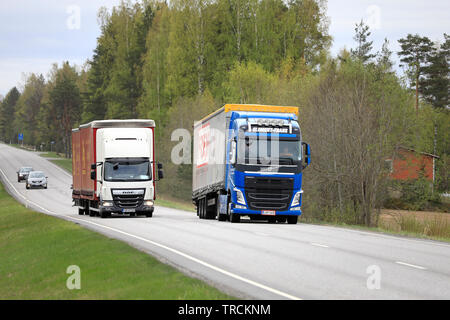 Salo, Finnland - 10. Mai 2019: Blaue Volvo FH truck Vor Sattelschlepper überholt Lkw ziehen voll Anhänger auf Landstraße im Süden Finnlands.