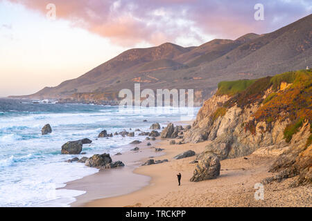 Mit Blick auf einen wunderschönen Sandstrand mit man zu Fuß am Strand entlang mit der hügelige Küste von Big Sur, Kalifornien in den Hintergrund. Stockfoto