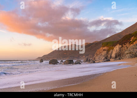 Sonnenuntergang an einem Sandstrand mit Bergen im entlang der Küste in Big Sur, Kalifornien. Stockfoto