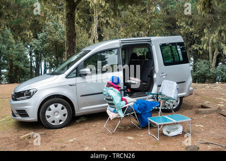 Frau liest neben kleinen Wohnmobil in einem Pinienwald Campingplatz in Spanien. Stockfoto