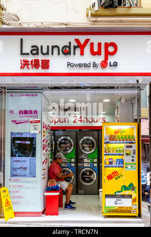 Ein Mann sitzt in einem Waschsalon und wartet auf seine Kleidung zu waschen, Hongkong, China Stockfoto