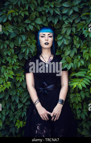 Schöne Goth Girl mit hellen blauen Haare stehen im Grünen Efeu. Am Vorabend von Halloween Stockfoto