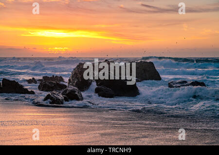 Big Sur, Kalifornien - schönen Sonnenuntergang am California Beach mit großen Wellen, die über Felsen und eine Schar Vögel in der Ferne fliegen. Stockfoto