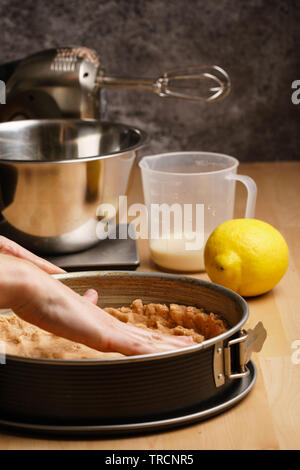 Zwei weiblichen kaukasischen Hände aus den rohen Teig verteilt in einem schwarzen Backblech, backen Geschirr in den Hintergrund - Seitenansicht, Hochformat Stockfoto