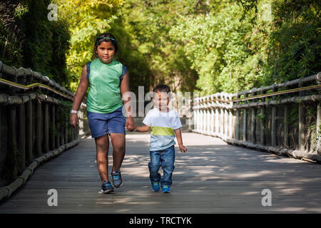 Große Schwester und Bruder zusammen gehen, Hände auf dem Bambus umgeben weg während des Sonnenuntergangs. Stockfoto