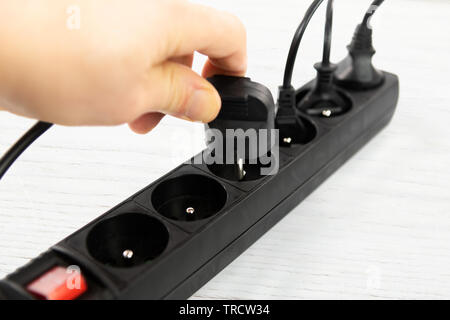 Energiesparkonzept - eine männliche Hand zieht einen elektrischen Stecker von einem Steckdosenleiste in Nahaufnahme. Stockfoto
