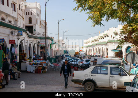 Hauptstraße von Moulay Idriss an einem sonnigen Tag, mit weißen Häusern, Läden, Bars und geparkte Autos. Moulay Idriss Zerhoun, Marokko. Stockfoto