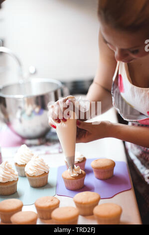 Frau, Frischkäse top auf Cupcakes in der Küche. Kochen Kuchen. Selektive konzentrieren. Stockfoto