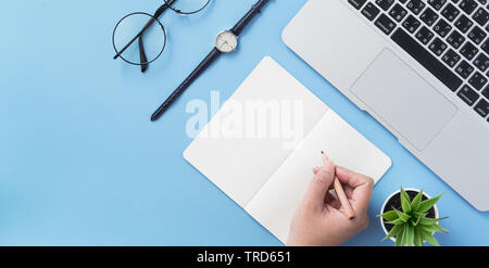 Mädchen schreibt am geöffneten weißen Buch oder auf einer minimalen sauber Hellblau Schreibtisch mit Laptop und Zubehör, Kopieren, Flach, Ansicht von oben, Mock up Stockfoto