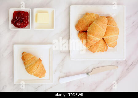 Frisch gebackene buttrige Croissants mit Butter und flockig Kirsche Konfitüre auf Marmor Hintergrund in Flach Komposition. Stockfoto