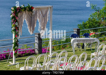 Hochzeit arch im Boho Stil in der Nähe des Ozeans mit macrame und frische Blumen, Sesseln, Tisch und Blütenblatt Gang für eine Zeremonie. Bali. Stockfoto