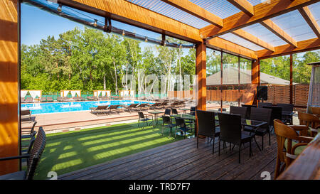 Sommer leer Outdoor Cafe im Park. Bar - Cafe mit einem modernen Design, hölzerne Wände, Stühle, Tische, im Hintergrund einen Pool und Liegestühle Stockfoto