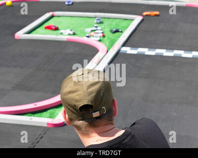 Kerl in Grüne Baseball Cap und Schwarzes T-Shirt Uhren Spielzeug Fernsteuerung Rennwagen auf der Strecke in der Veranstaltung. Stockfoto