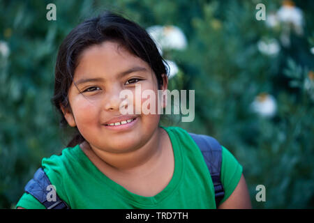 Cute elementary Student mit Rucksack vor Grün Blumen mit einer positiven Einstellung und natürliches Aussehen. Stockfoto