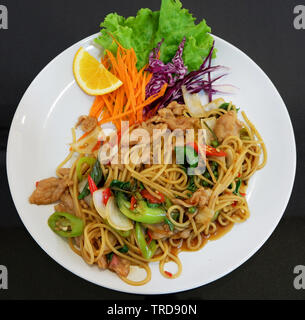 Gebratene Nudeln spaghetti pikanter Chili Schwein und grünem Pfeffer Saatgut mit frischem Gemüse auf dem Teller und dunklen Hintergrund rühren Stockfoto