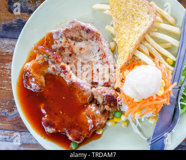 Gegrilltes Steak vom Schwein Pommes frites Salat Gemüse mit Steak Sauce auf dem Teller auf dem Tisch Stockfoto
