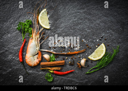 Garnelen Garnelen Gekochte Schalentiere Meeresfrüchte mit Zitronen Tomaten Kräuter und Gewürze auf dunklem Hintergrund Stockfoto