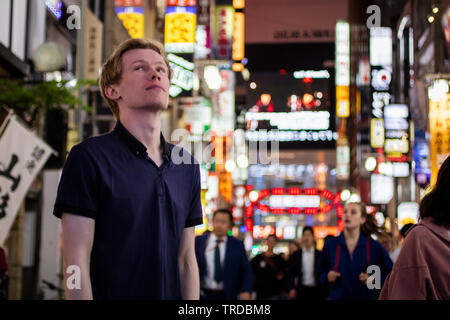 Einen gutaussehenden blonden Touristen auf der Suche von der Seite auf einem neon Tokyo street Stockfoto
