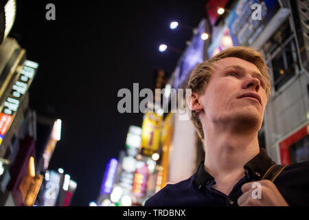 Einen gutaussehenden blonden Touristen auf der Suche von der Seite auf einem neon Tokyo street Stockfoto