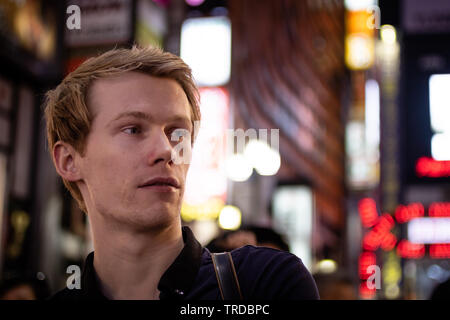 Einen gutaussehenden blonden Touristen auf der Suche von der Seite auf einem neon Tokyo street Stockfoto