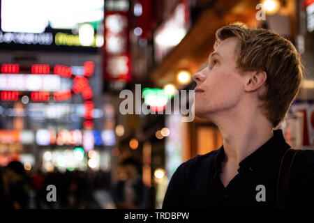 Einen gutaussehenden blonden Touristen auf der Suche von der Seite auf einem neon Tokyo street Stockfoto
