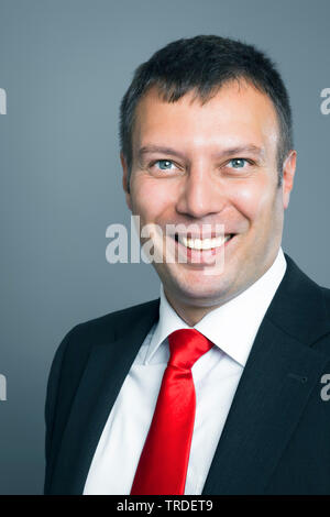 Porträt eines sympathischen, Lächeln, Geschäftsmann, der in einen schwarzen Anzug gegen grauer Hintergrund Stockfoto