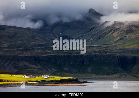 Bauernhaus in der Sonne vor der dunklen Bergwelt, Island, Snaefellsnes, Grindafjoerdur Stockfoto