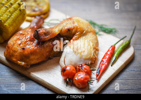 Gebratene Hähnchenschenkel auf Holz Schneidebrett mit Mais lemon Chili würzige Kräuter, Gewürze und Tomaten am Esstisch Essen/gegrillte Hähnchen Stockfoto