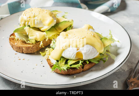 Eier Benedikt mit Salat und Avocado auf konkreten Hintergrund. Stockfoto