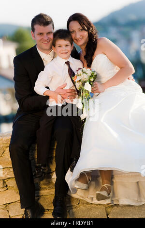 Hochzeit Bild von einem Brautpaar mit einem Kind sitzen auf einer Mauer aus Stein Stockfoto