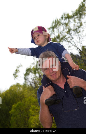 Portrait einer jungen Junge sitzt auf seinem Vater ┤ s Schulter und Richtung etwas Stockfoto