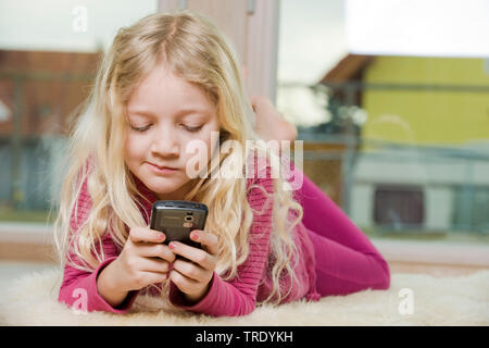 Porträt eines Mädchens auf dem Boden liegen und das Spielen mit Ihrem Mobiltelefon Stockfoto