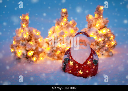 Santa Claus und kleine Beleuchtete Weihnachtsbäume im Schnee Stockfoto