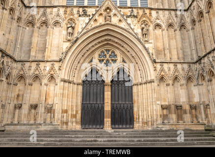 Die zentrale nach Westen Türen Münster von York. Steinstufen führen bis zu zwei dekorative hölzerne Flügeltüren. In einem archivolte, eine Figur oben ist. Stockfoto