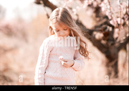 Süße blonde Kind Mädchen 5-6 Jahre alten Stand im Freien. Holding Blume über die Natur Hintergrund. Tragen stilvolle rosa Pullover. Kindheit. Stockfoto