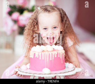 Lachen kind Mädchen essen Geburtstag Kuchen mit offenen Mund closeup im Zimmer. Mit Blick auf die Kamera. Kindheit. Stockfoto