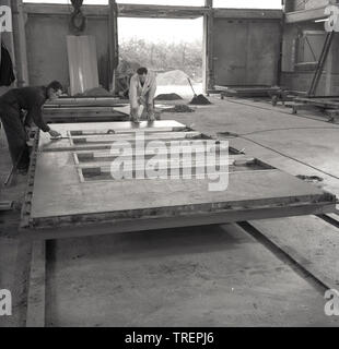 1960s, historisch, Arbeiter in einer Industrieeinheit mit einer neuen vorgegossenen Betonplatte, England, Großbritannien. In dieser Zeit wurden vorgegossene Betonplatten im Bau großer Büro- und Turmblöcke aus Gründen der geringeren Kosten und der Schnelligkeit der Konstruktion mit dem architektonischen Stil, der als „Modernismus“ oder „Brutalismus“ bekannt ist, weit verbreitet. Stockfoto