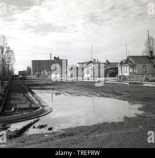 1960s, historisch, eine breite, neu gebaute, unbewaffelte Straße, Mit einer großen Pfütze an der Ecke, Anchorage, Alaska, USA. Stockfoto