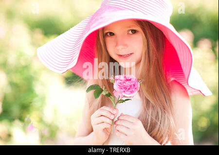 Lächelnd Cute Baby Mädchen 4-5 Jahre alten Holding Blume tragen einen großen Hut in der Wiese. Mit Blick auf die Kamera. Kindheit. Sommer. Stockfoto