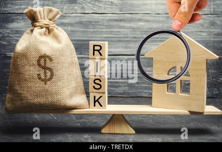 Geld beutel, Blöcke mit dem Wort Risiko und ein Holzhaus auf der Waage. Das Konzept, Geld zu verlieren, wenn Sie in Immobilien investieren. Risiken der Verlust eines Ho Stockfoto