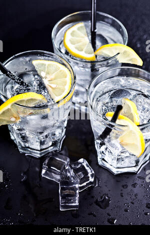 Drei Gläser mit frischem, kaltem Wasser mit Kohlensäure mit Zitronenscheiben und Eiswürfel Nahaufnahme. Sodawasser auf schwarzem Hintergrund. Stockfoto