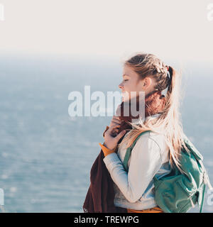 Lächelnd jugendlich Mädchen 14-16 Jahre alten Reisen mit Rucksack über Meer Hintergrund. Tragen warmer Schal, gestrickte Pullover und Jeans Jacke. Stockfoto