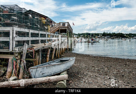 New England Fishing Port: ein kleines Boot wartet neben einer groben hölzerne Seebrücke hoch mit Hummer Traps an einer Bucht im Südosten Maine angehäuft. Stockfoto