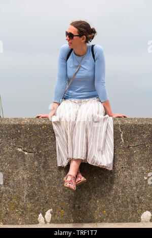 Frau in den frühen 40er/40er/40er Jahre sitzen auf der Mauer und lächelnd im warmen Sonnenschein. Sie trägt einen Rock, Sandalen und Sonnenbrille von der Sonne England UK (99) zu schützen Stockfoto