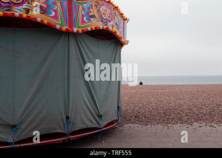 Eine einsame Person sitzen Am Strand von Brighton mit einem geschlossenen Messe Fahrt im Vordergrund. Stockfoto