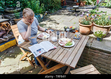 Eine Frau mit einem Frühstück unter freiem Himmel auf einem Suburban Garten Terrasse an einem schönen Sommermorgen, London, UK Stockfoto