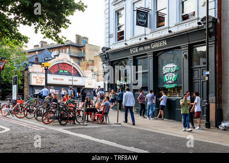 Trinker außerhalb der Fuchs auf dem Grün Pub im Islington Green, London, UK, der Bildschirm auf dem Grünen Kinos in ganz obere Straße im Hintergrund Stockfoto