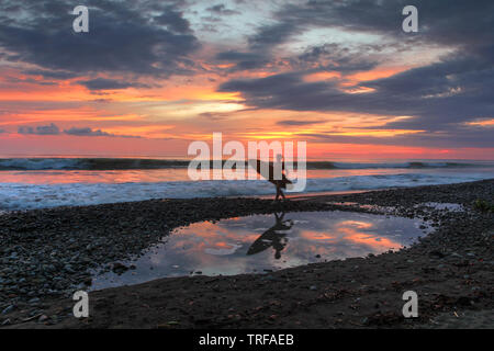 Playa Dominical in Costa Rica ist ein felsiger Strand meist durch ausländische Surfer abgerechnet. Sonnenuntergang Szene mit Surfer, Wellen und der untergehenden Sonne. Stockfoto