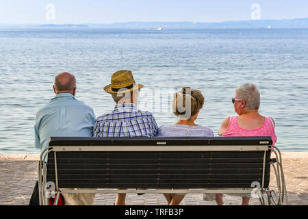 Gardasee, Italien - September 2018: Vier Personen sitzen auf einer Bank am Ufer des Gardasees. Stockfoto